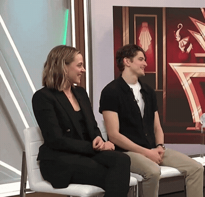 Man And Woman Sitting In Front Of Red Wall GIF
