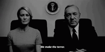 Man And Woman Sitting In Front Of Sign Saying We Make The Terror GIF