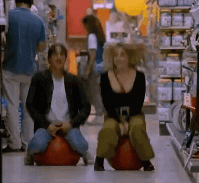 Man And Woman Sitting On Bouncy Balls In Grocery Store GIF