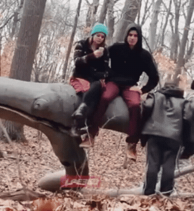 Man And Woman Sitting On Dinosaur Statue GIF