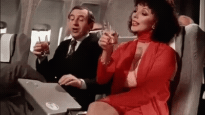 Man And Woman Sitting On Plane Holding Wine GIF