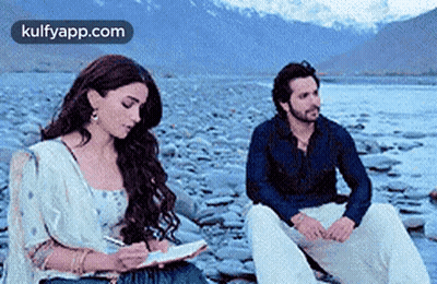Man And Woman Sitting On Rocky Beach Woman Writing In Notebook GIF