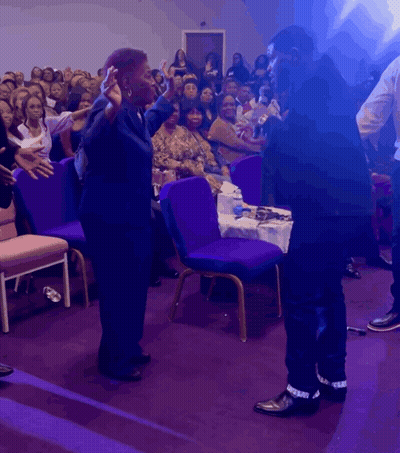 Man And Woman Stand Before Crowd In Purple Chairs GIF