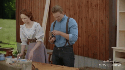 Man And Woman Standing Beside Hallmark Movies Now Table GIF