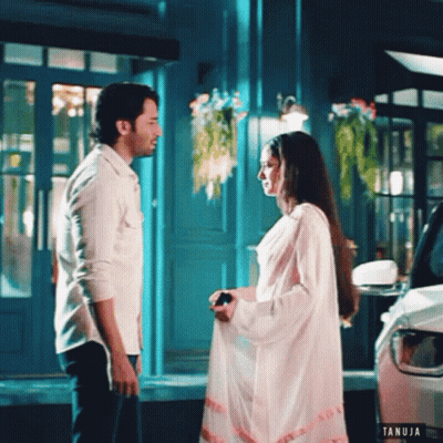 Man And Woman Standing In Front Of Building With Tanuja Logo GIF