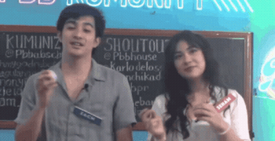 Man And Woman Standing In Front Of Shoutout Sign GIF
