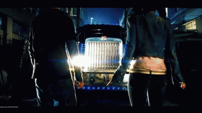 Man And Woman Standing In Front Of Transformers Semi Truck GIF
