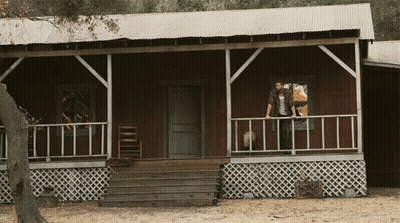 Man And Woman Standing On Porch Of Wooden House GIF