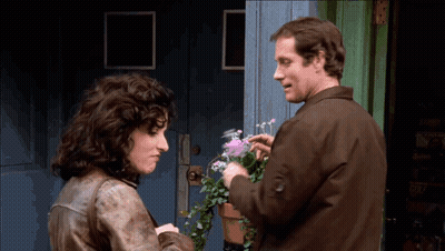 Man And Woman Talking About Flowers In Front Of Blue Door GIF