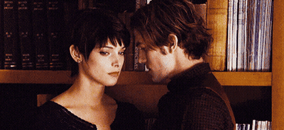 Man And Woman Touching Foreheads In Front Of Bookshelf GIF