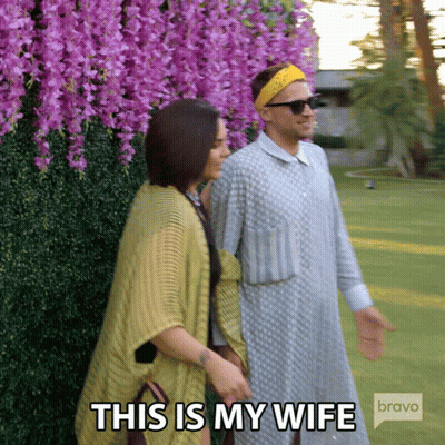 Man And Woman Walking In Front Of Purple Flowers Saying This Is My Wife Bravo GIF