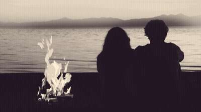 Man And Woman Watching Fire On Lake Shore GIF