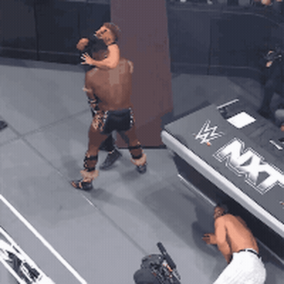 Man And Woman Wrestling In Front Of NXT Sign GIF