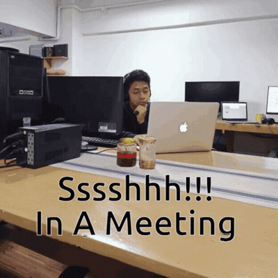 Man At Desk With Apple Laptop Saying Shhh In Meeting GIF