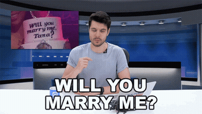 Man At Desk With Sign Saying Will You Marry Me Tana GIF