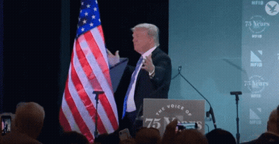 Man At Podium With Sign Saying The Voice Of 75 Years GIF
