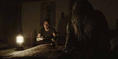 Man At Table In Dark Room With Lantern GIF