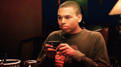 Man At Table Looking At Phone In Chris Brown Shirt GIF
