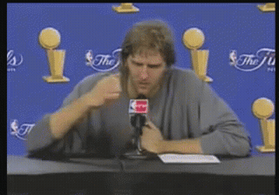 Man At Table With Microphone In Front Of NBA Trophies GIF