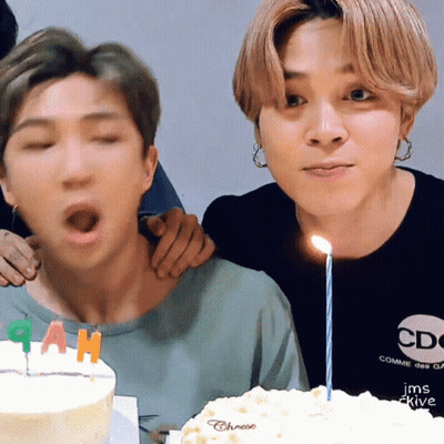 Man Blowing Out Candle On Cake While Another Man Watches GIF