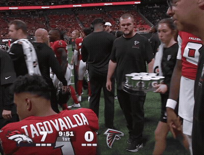 Man Carrying Beer Tray Past Man In Falcons Uniform GIF