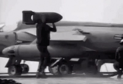 Man Carrying Large Bomb On Head In Front Of Jet GIF