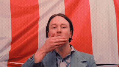 Man Covering Mouth In Front Of Red White Blue Flag GIF