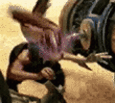 Man Doing Handstand In Sand While Another Holds Purple Object GIF