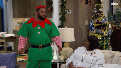 Man Dressed As Elf Standing Next To Woman On Couch GIF