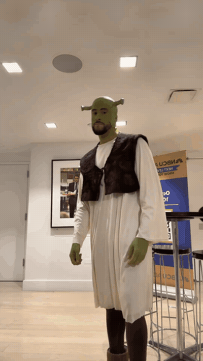 Man Dressed As Shrek In Front Of UCB Sign GIF