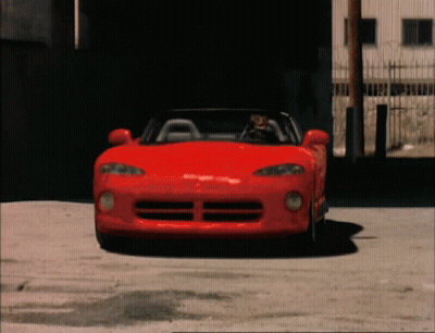 Man Driving Red Sports Car In Front Of Building GIF