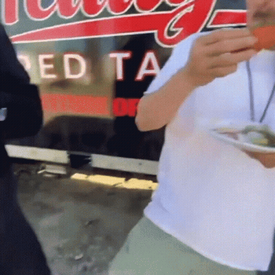Man Eating Food In Front Of Red Ta Sign GIF