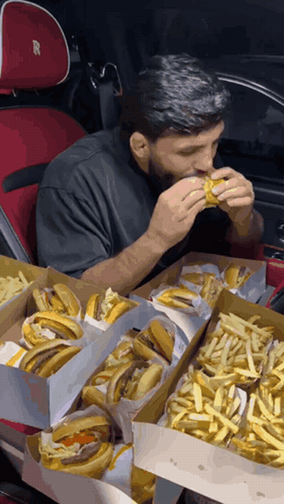Man Eating Hamburger In Car With Boxes Of Hamburgers And French Fries GIF