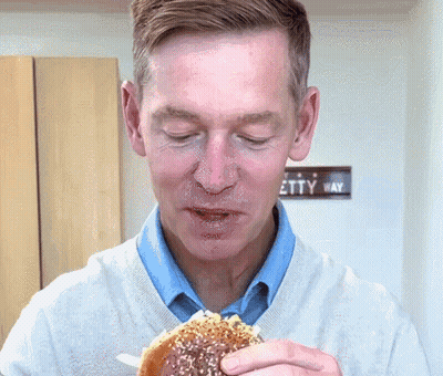 Man Eating Hamburger In Front Of Etty Way Sign GIF