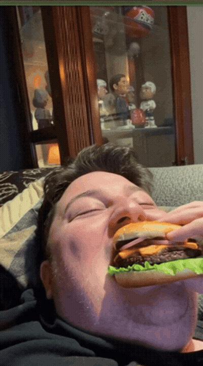 Man Eating Hamburger With Bobble Head Saying BB GIF