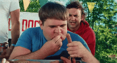 Man Eating Hot Dog Beside Sign Saying Dog GIF