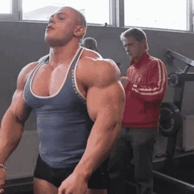 Man Flexing Muscles While Man In Red Jacket Watches GIF