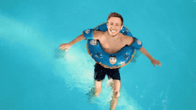 Man Floating In Pool With Blue Shark Tube GIF
