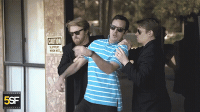 Man Held By Two Men In Front Of Caution Slippery When Wet Sign GIF