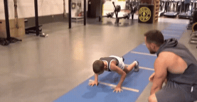 Man Helping Boy Do Push Ups On Blue Mat In Gym GIF