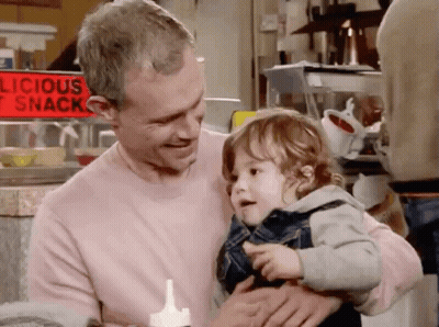 Man Holding Baby in Front of Delicious Snack Sign