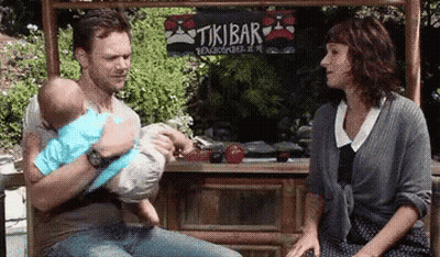 Man Holding Baby In Front Of Tikibar GIF