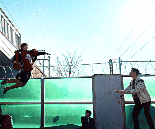 Man Holding Basketball Jumping Over Fence GIF