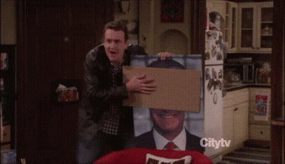 Man Holding Cardboard Box With Man Picture In Front Of Citytv Refrigerator GIF