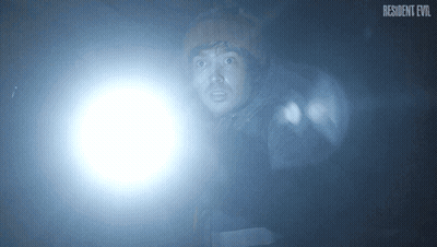 Man Holding Flashlight In Dark Room With Resident Evil Logo GIF