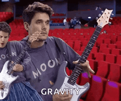 Man Holding Guitar In Front Of Red Seats Says Gravity GIF