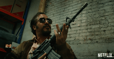 Man Holding Gun In Front Of Brick Wall With Netflix Logo GIF
