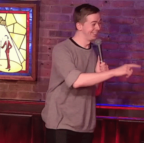 Man Holding Microphone In Front Of Brick Wall Pointing GIF