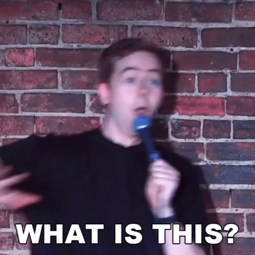 Man Holding Microphone In Front Of Brick Wall Saying What Is This GIF
