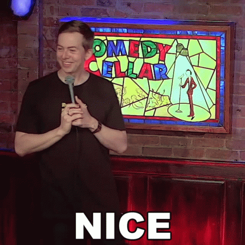 Man Holding Microphone In Front Of Comedy Cellar Sign GIF